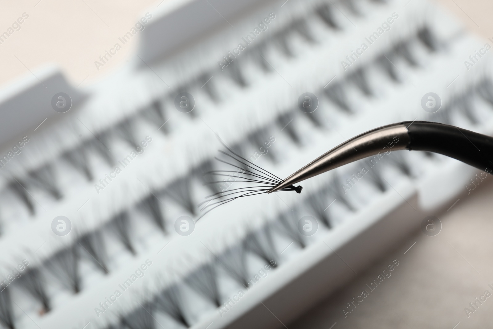 Photo of Tweezers with bunch of artificial eyelashes on blurred background, closeup. Space for text