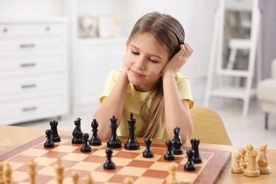 Cute girl playing chess at table in room