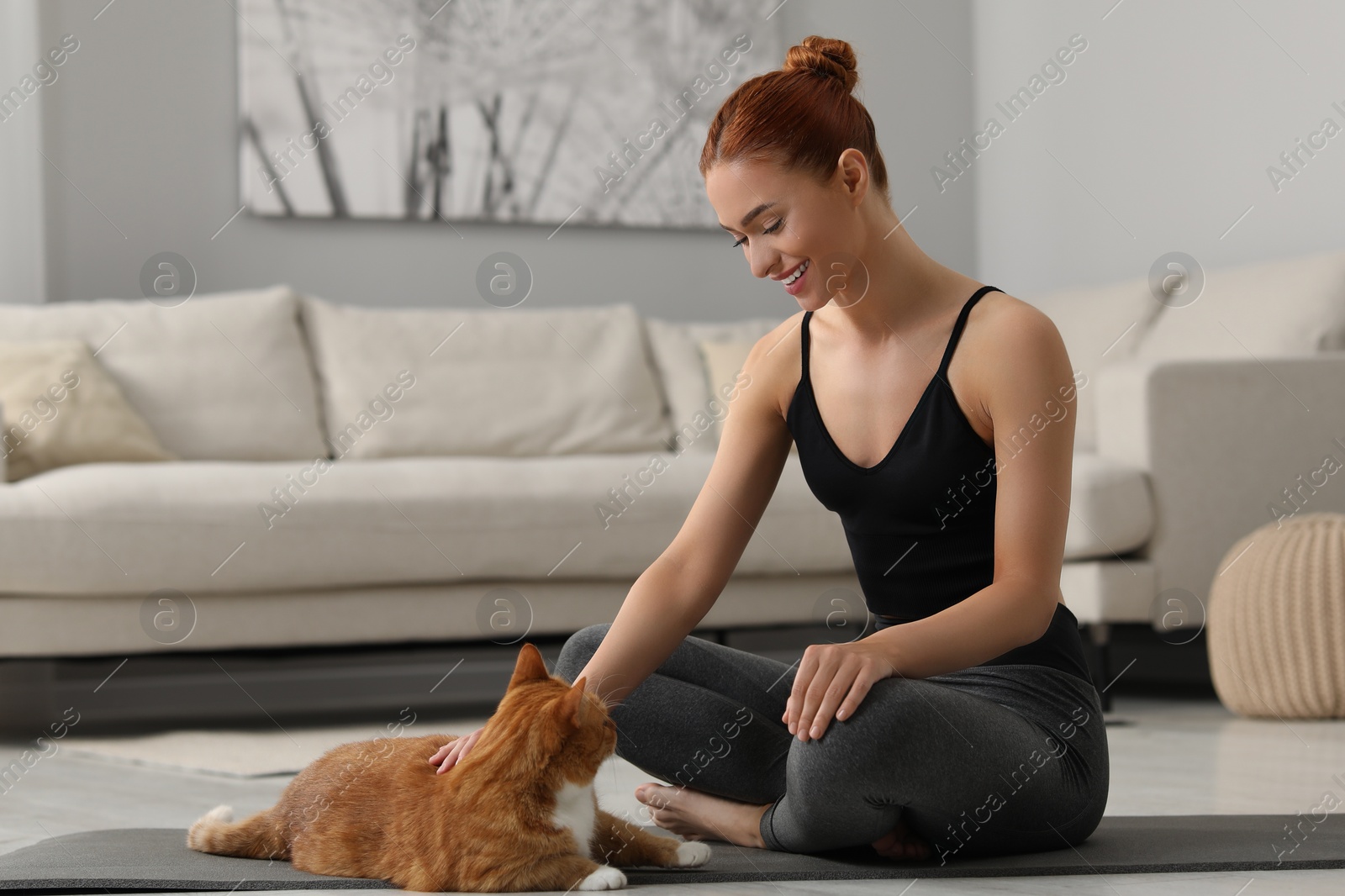 Photo of Beautiful woman petting cute red cat on mat at home. Practicing yoga