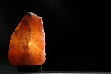 Photo of Himalayan salt lamp on black background. Space for text