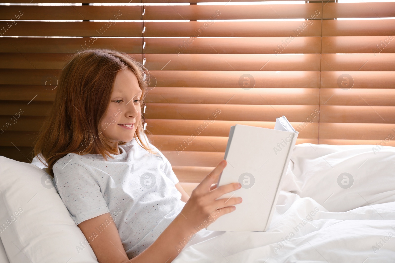 Photo of Cute preteen girl reading book in bed near window