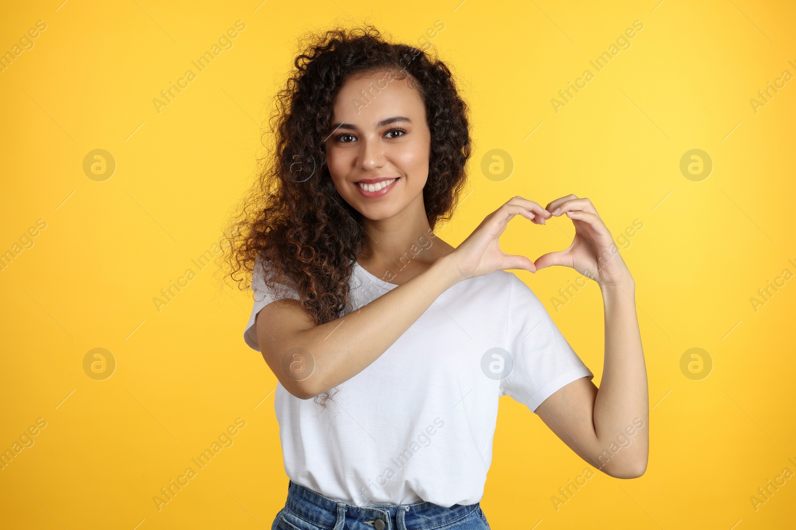 Photo of Happy young African-American woman making heart with hands on yellow background