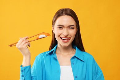Photo of Happy beautiful young woman holding sushi with chopsticks on orange background
