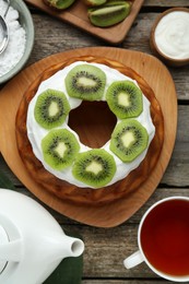 Homemade yogurt cake with kiwi, cream and aromatic tea on wooden table, flat lay