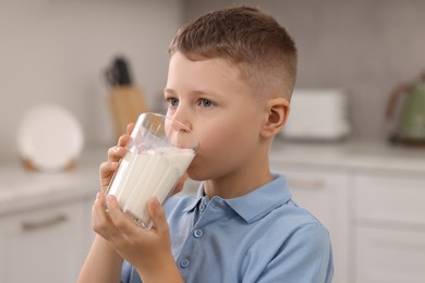 Photo of Cute boy drinking fresh milk from glass indoors