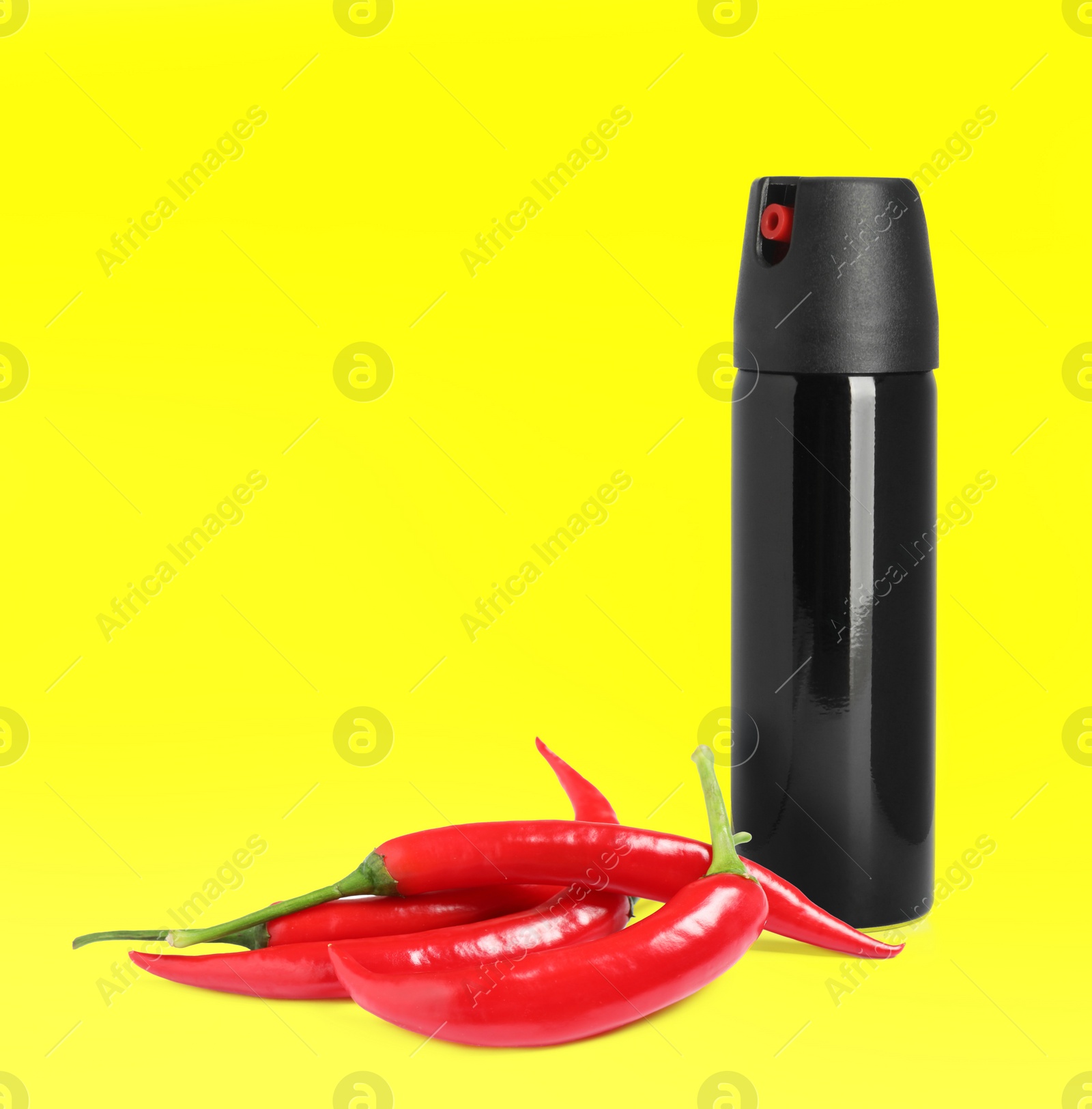 Image of Bottle of pepper spray and red hot chilies on yellow background