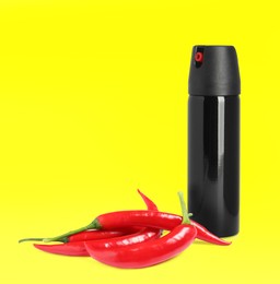 Image of Bottle of pepper spray and red hot chilies on yellow background