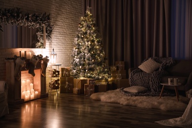 Photo of Stylish interior with beautiful Christmas tree and artificial fireplace at night