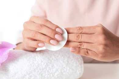 Photo of Woman removing polish from nails with cotton pad at table, closeup
