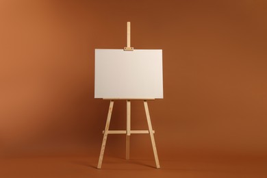 Photo of Wooden easel with blank canvas on brown background