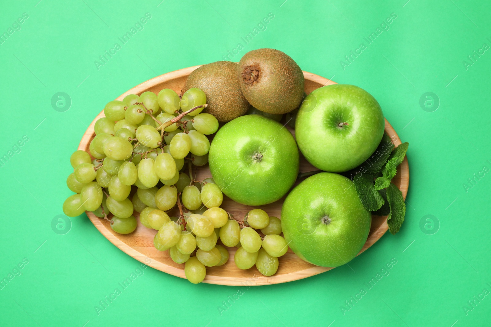 Photo of Fresh ripe apples, kiwis, grape and mint on green background, top view