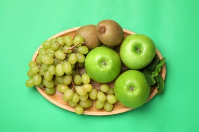 Photo of Fresh ripe apples, kiwis, grape and mint on green background, top view