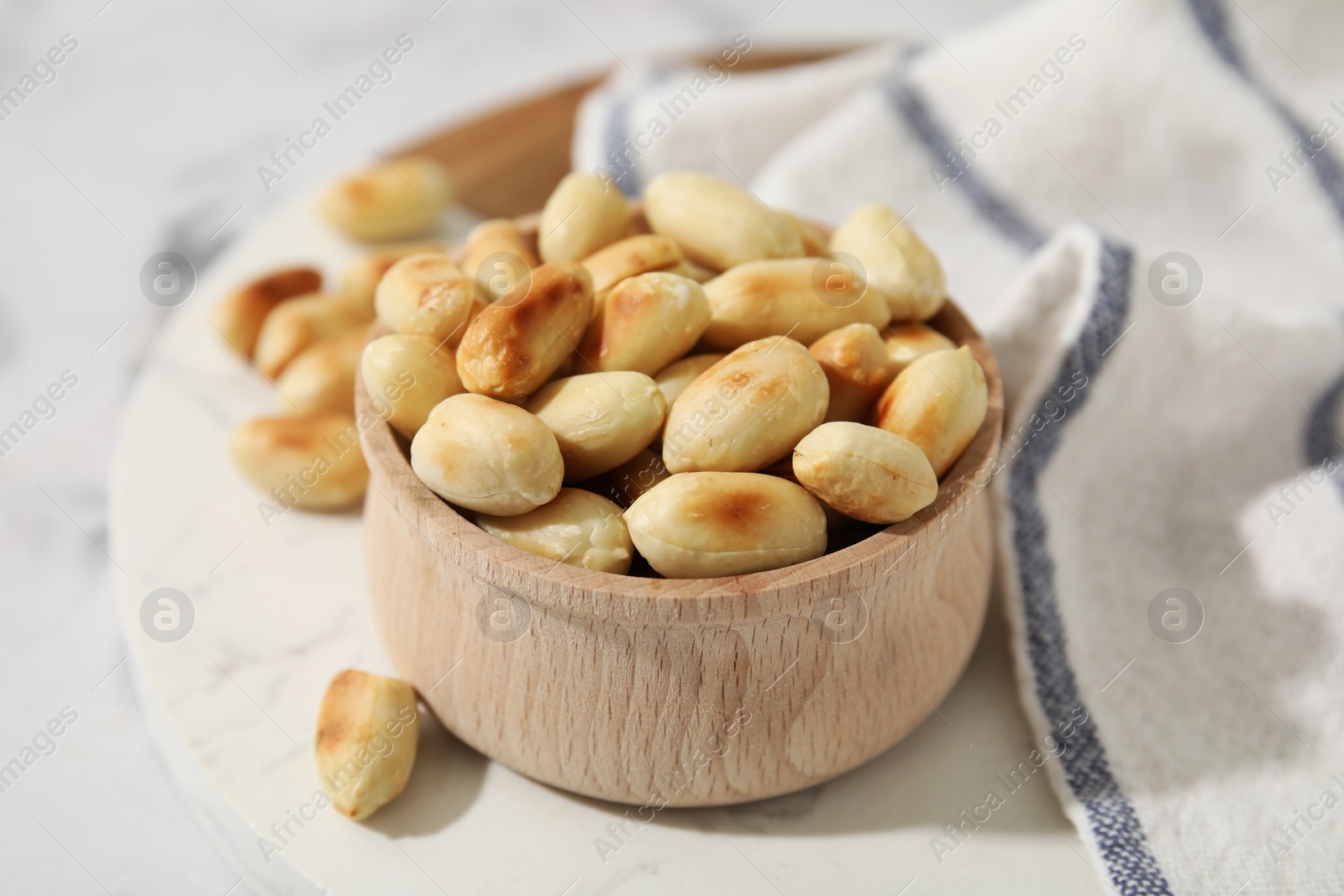 Photo of Roasted peanuts in bowl on white table, closeup