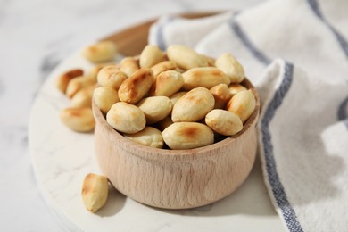 Roasted peanuts in bowl on white table, closeup