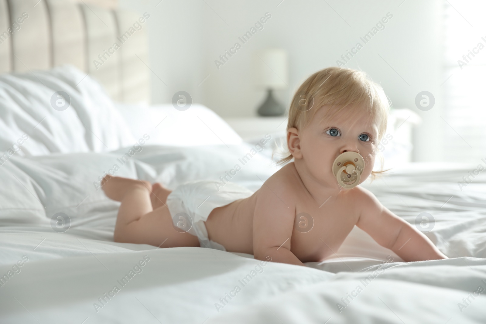 Photo of Cute little baby in diaper with pacifier lying on bed at home