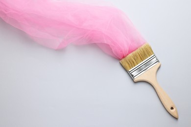 Photo of Brush painting with pink tulle on light background, top view. Creative concept