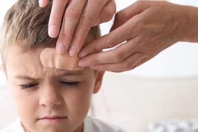 Photo of Woman applying adhesive bandage on boy's forehead indoors, closeup