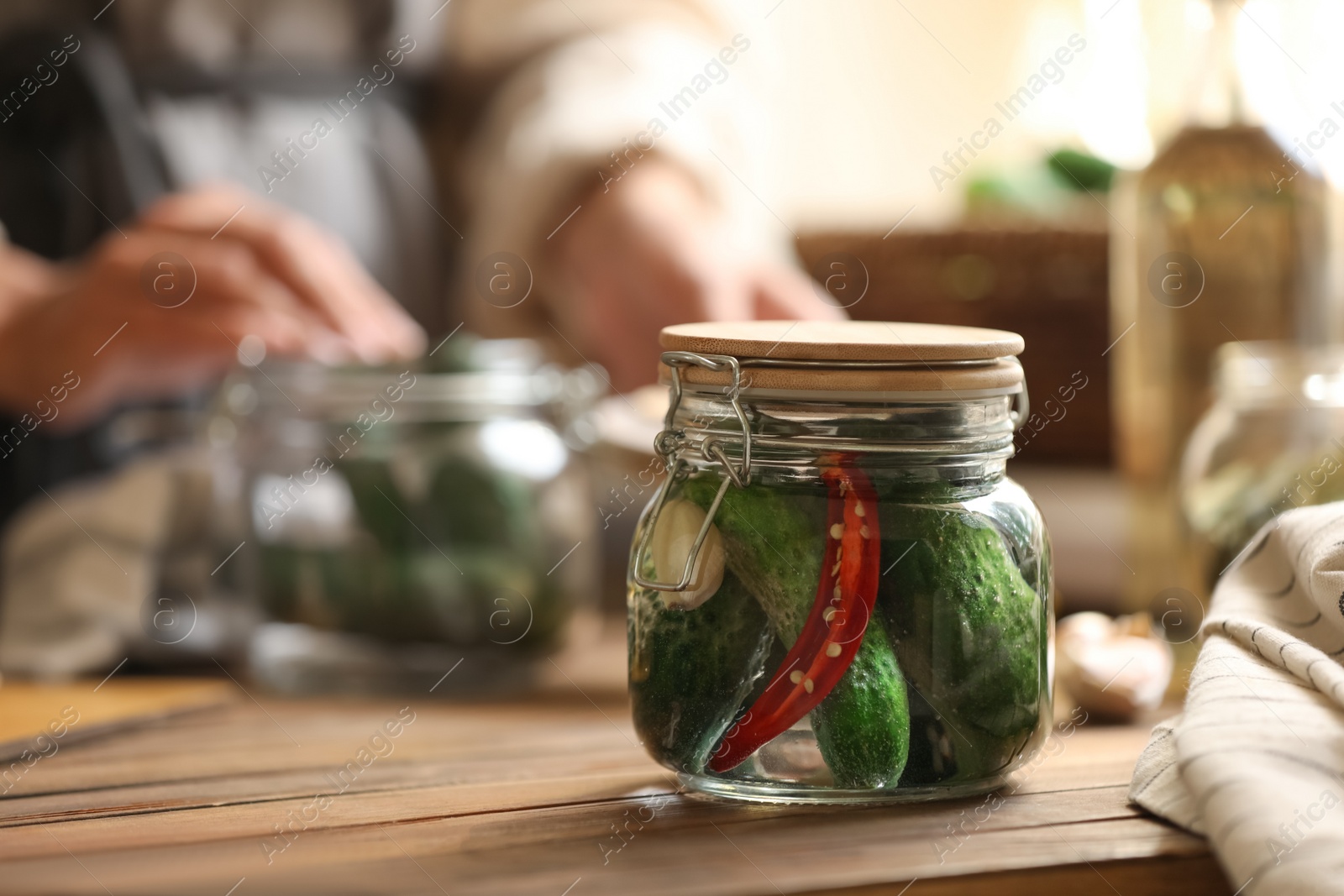 Photo of Woman pickling vegetables at table indoors, focus on jar with cucumbers