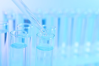 Photo of Dripping liquid from pipette into test tube on light blue background, closeup