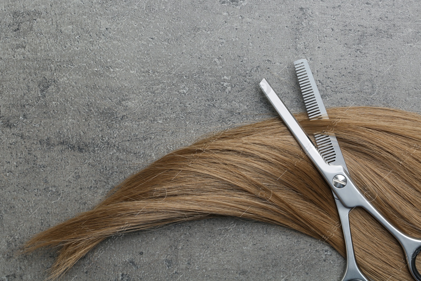 Photo of Flat lay composition with light brown hair, thinning scissors and space for text on grey background. Hairdresser service