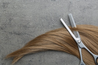 Flat lay composition with light brown hair, thinning scissors and space for text on grey background. Hairdresser service