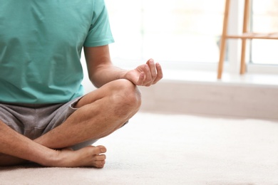 Photo of Man meditating on floor at home, closeup with space for text. Zen concept
