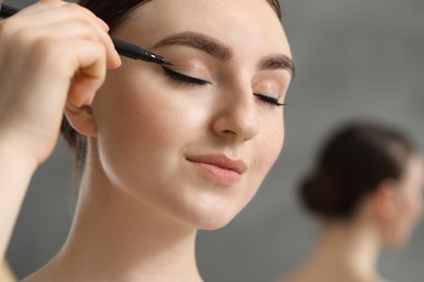 Makeup product. Woman applying black eyeliner on blurred background, closeup