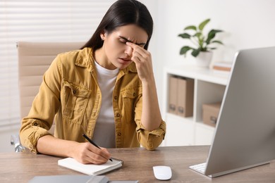 Photo of Young woman suffering from headache at wooden table in office