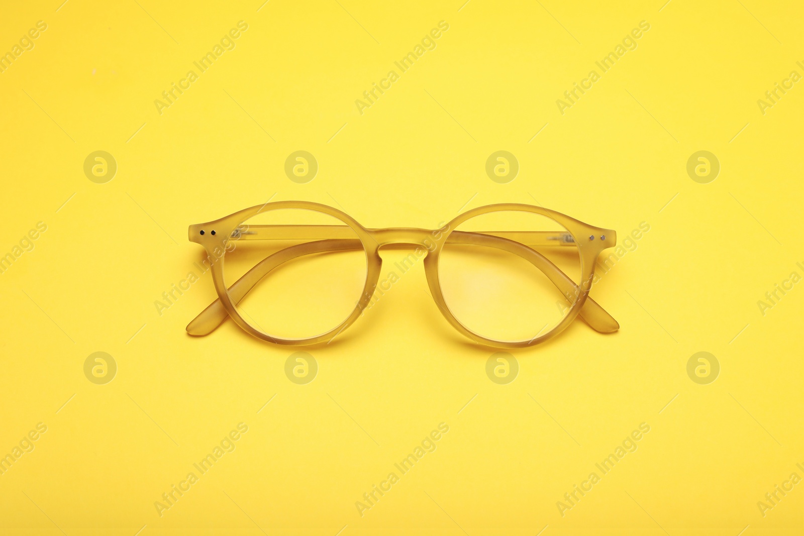 Photo of Glasses with corrective lenses on yellow background, top view