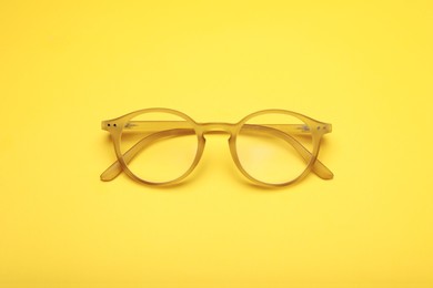 Photo of Glasses with corrective lenses on yellow background, top view