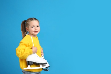 Cute little girl in yellow knitted sweater with ice skates on blue background, space for text
