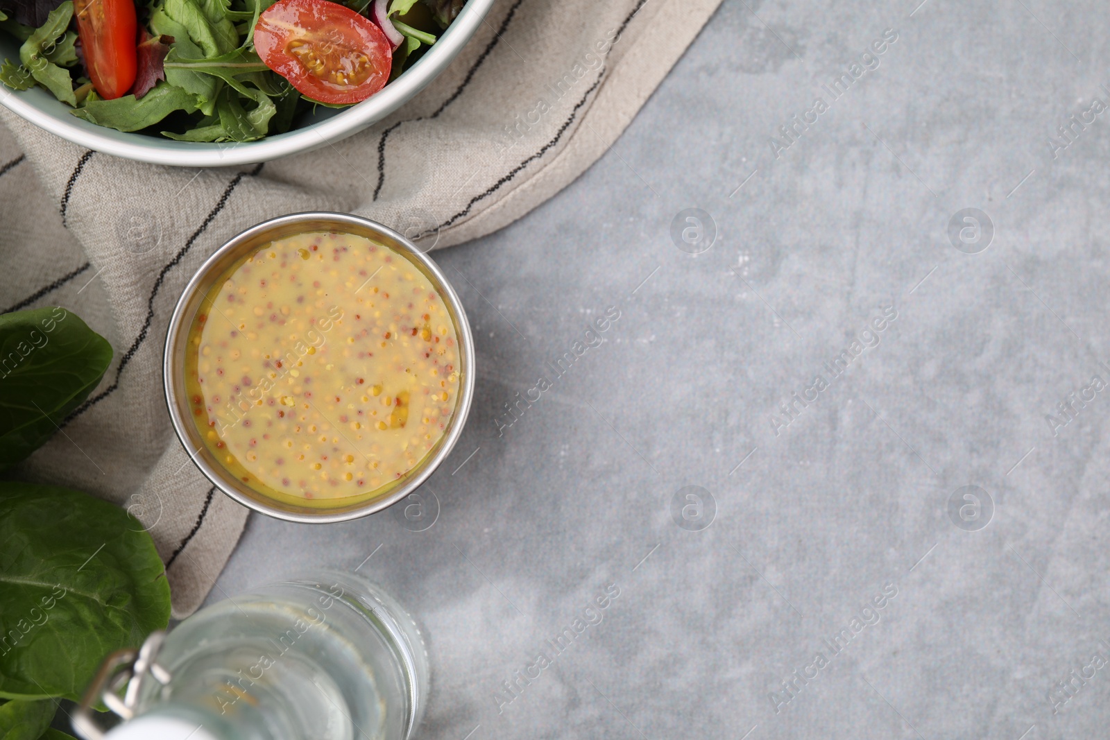 Photo of Tasty vinaigrette in bowl, vinegar and salad on grey table, flat lay. Space for text