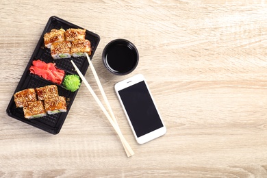 Photo of Flat lay composition with sushi rolls and smartphone on wooden table, space for text. Food delivery