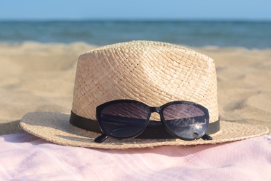 Photo of Hat with beautiful sunglasses on blanket near sea, closeup