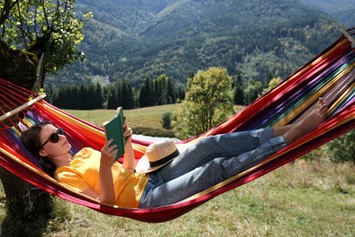 Photo of Young woman reading book in hammock outdoors on sunny day