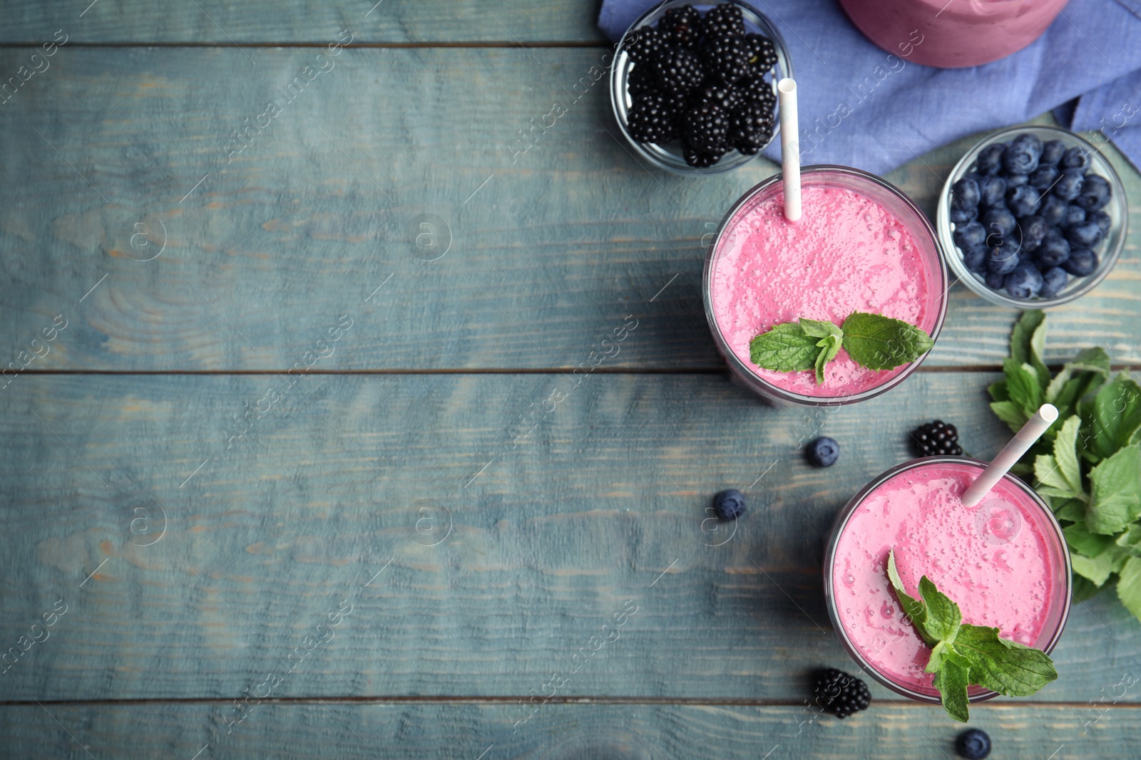 Photo of Tasty fresh milk shakes with berries on light blue wooden table, flat lay. Space for text