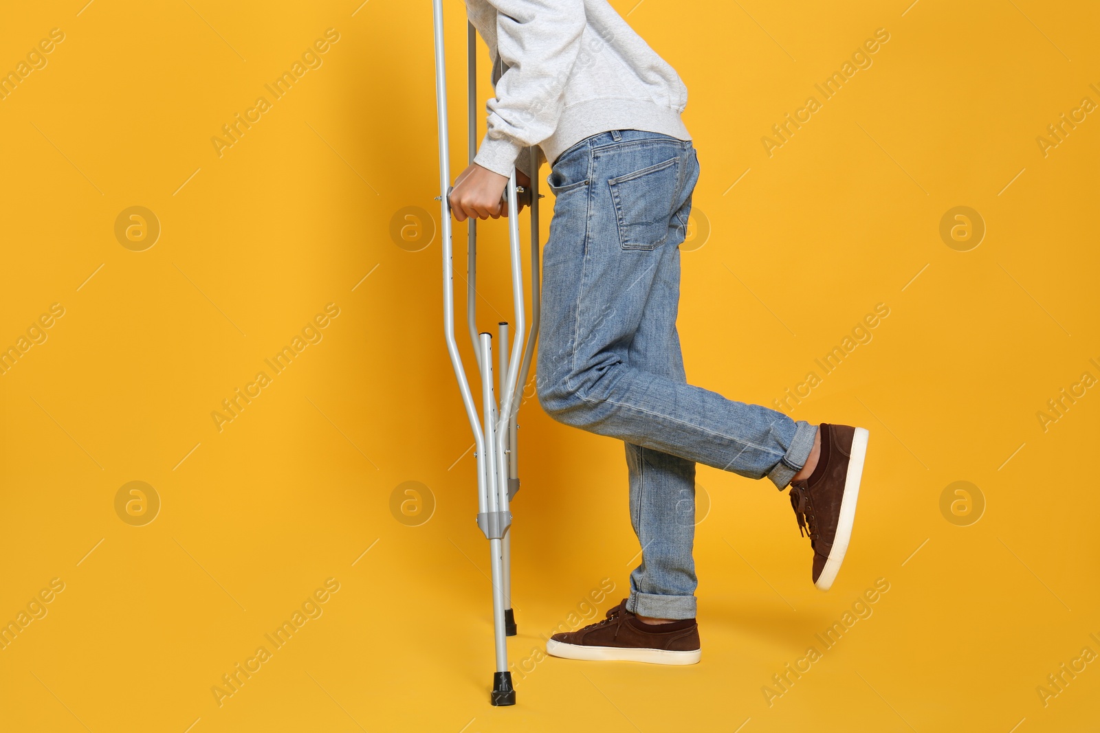 Photo of Man with injured leg using crutches on yellow background, closeup