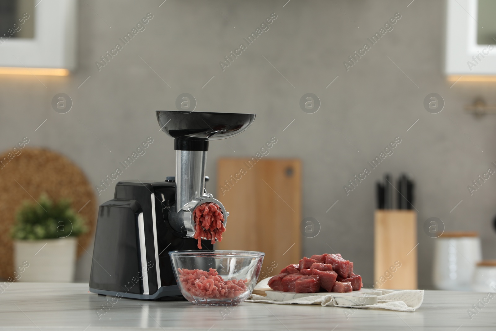 Photo of Electric meat grinder with beef mince on white table in kitchen, space for text