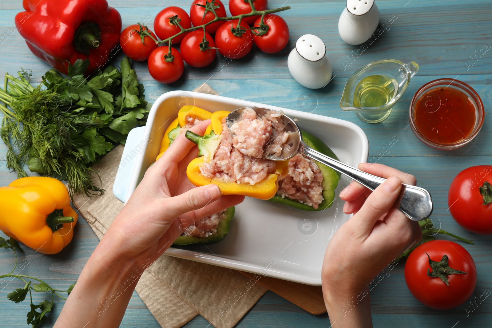 Photo of Woman making stuffed peppers with ground meat at light blue wooden table, top view
