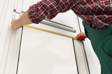 Photo of Worker using measuring tape while installing roller window blind indoors, closeup
