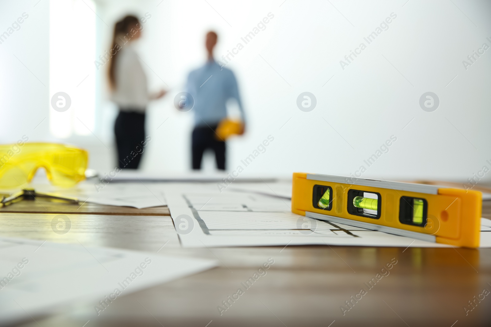 Photo of Colleagues in office, focus on table with construction drawings and tools