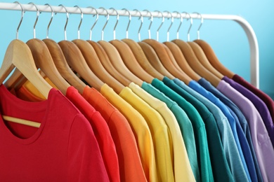 Rack with bright clothes on blue background. Rainbow colors