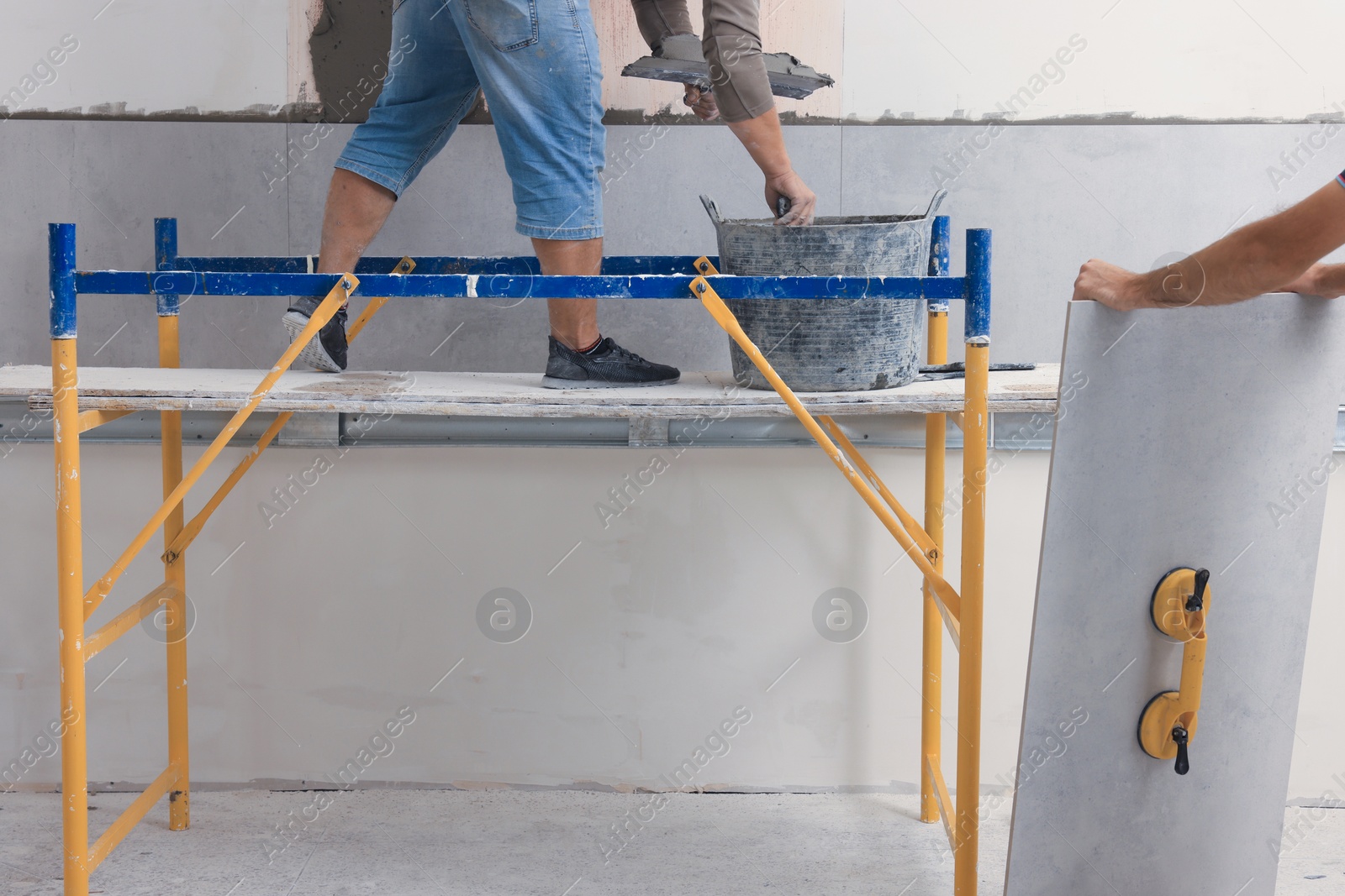 Photo of Worker installing ceramic tiles on wall indoors, closeup