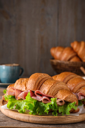 Photo of Tasty croissant sandwiches with ham on wooden table