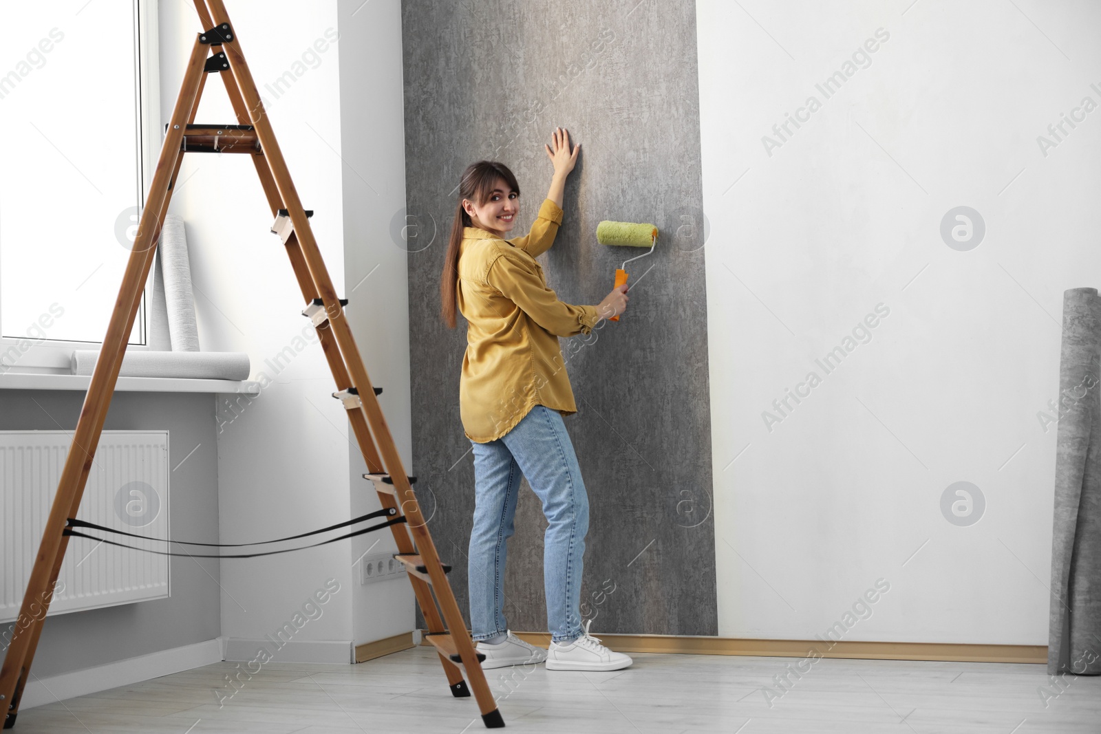 Photo of Woman hanging stylish gray wallpaper in room