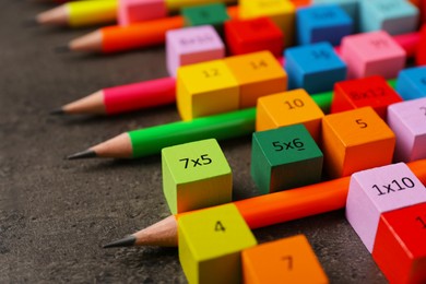 Photo of Many colorful cubes with numbers, multiplications and pencils on dark grey table, closeup
