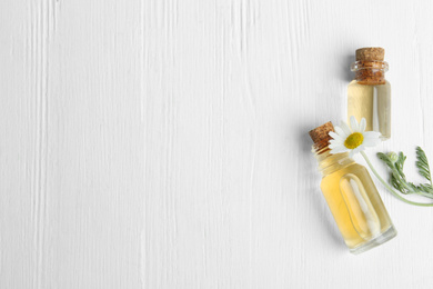 Photo of Bottles of essential oil and chamomile on white wooden background, flat lay. Space for text