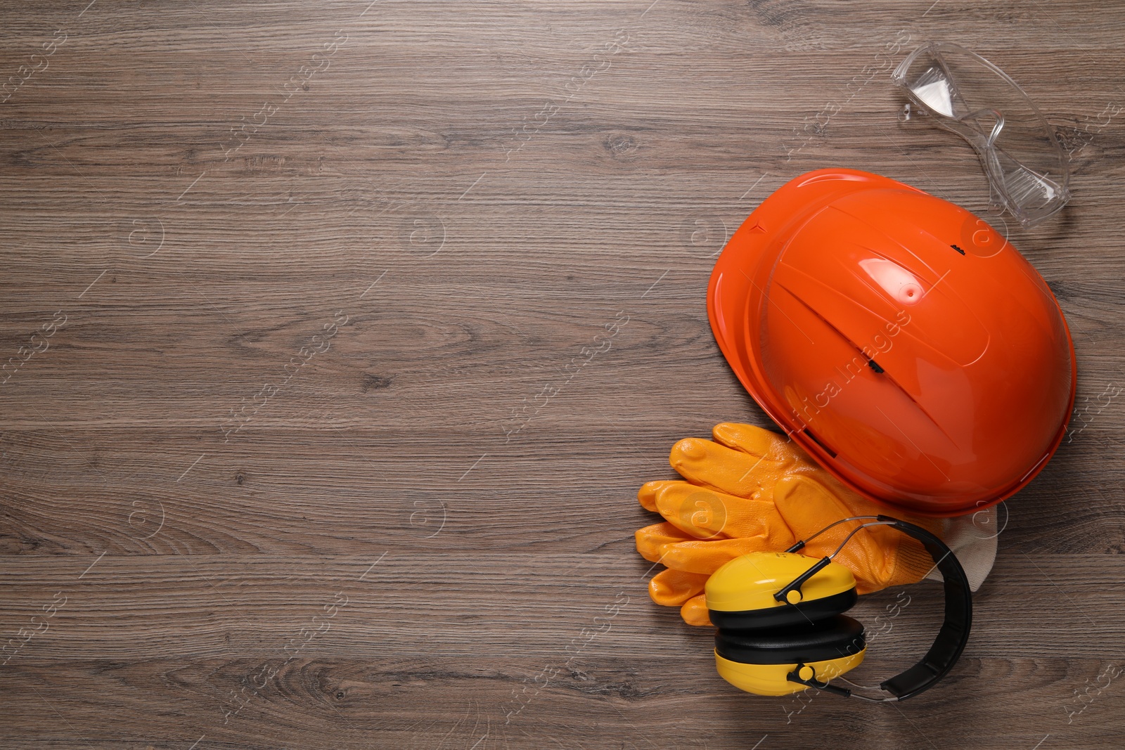 Photo of Hard hat, gloves, goggles and earmuffs on wooden table, flat lay with space for text. Safety equipment