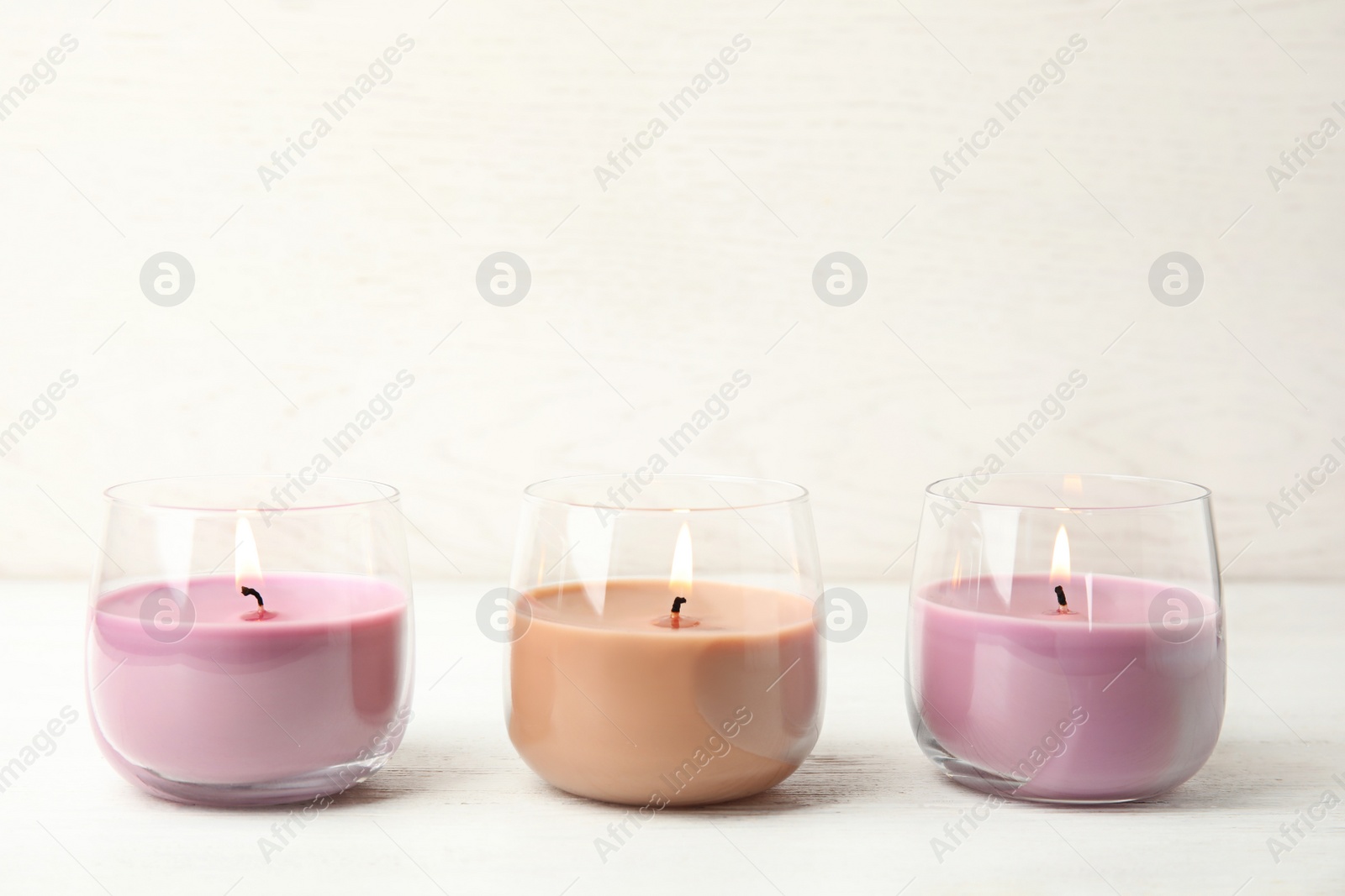 Photo of Color wax candles in glass holders on white table, space for text