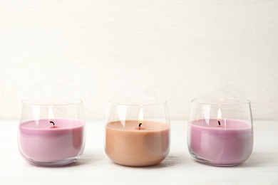 Color wax candles in glass holders on white table, space for text